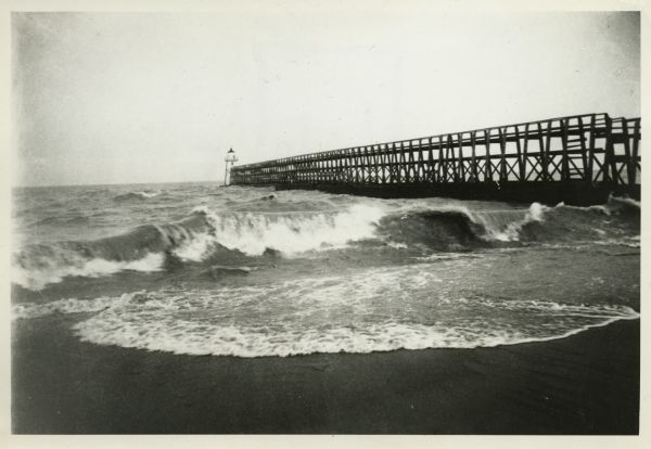 View from the shore of Kenosha's North Pier and lighthouse. Waves are breaking on the shore of Lake Michigan.