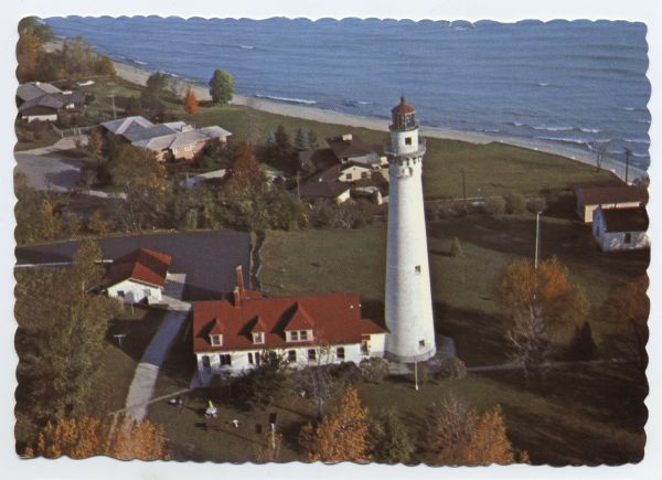 Aerial view of Wind Point lighthouse on the shore of Lake Michigan. A few neighboring homes are in the foreground. Some of the trees are displaying fall colors.