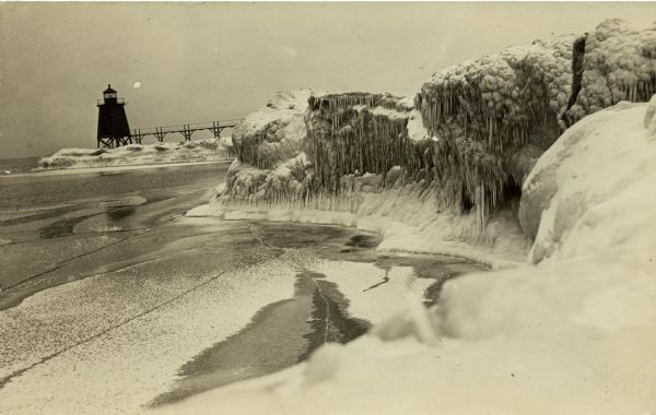 Postcard view along icy shoreline of the pier and lighthouse on Lake Michigan at Port Washington in winter.