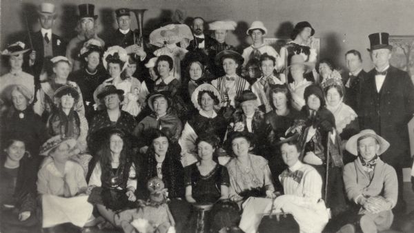 The library staff of the State Historical Society of Wisconsin and their guests the University of Wisconsin Library staff, at the Society's seventieth anniversary party. Most attendees are in 1840's period costume. The Society's Director, Milo Quaife is in the bottom right corner. Mr. Volk in the back row holds a horn.