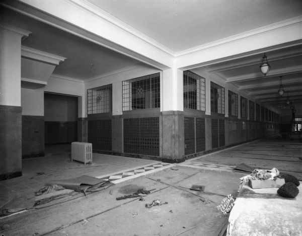 Interior view of first floor lobby with construction debris and some tile work completed on the floor. In the background a man is standing on a ladder near light fixtures hanging from the ceiling.