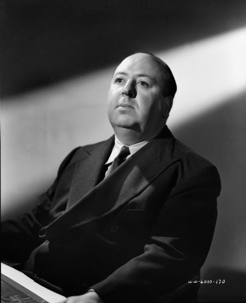 Publicity photograph of Alfred Hitchcock. He is seated and is wearing a suit and tie.