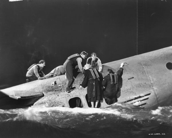 Six people crawl out of an airplane that is in the water. The scene is part of the film "Foreign Correspondent."