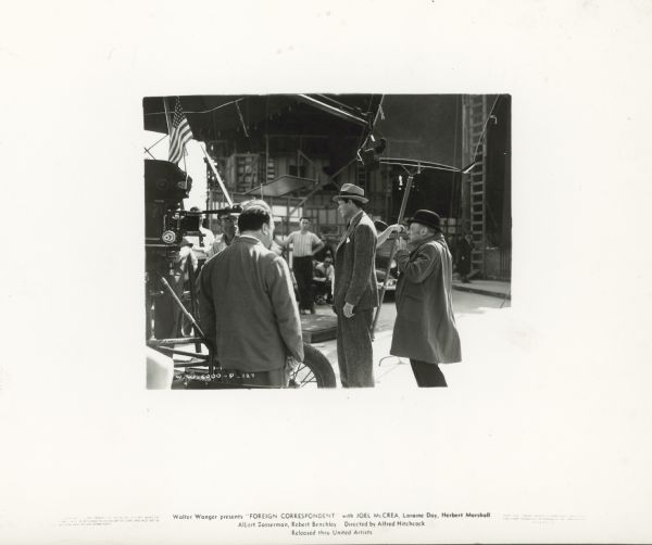 Joel McCrea and Alfred Hitchcock are seen with crew members on the set of the film "Foreign Correspondent."  An unidentified man stands behind McCrea making a face.   Hitchcock has his back to the camera.