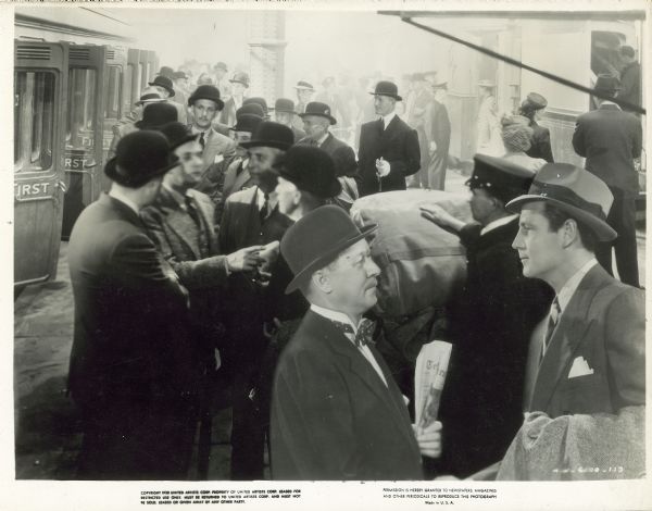 Joel McCrea and Robert Benchley greet each other at Waterloo Station in a scene still for the film "Foreign Correspondent." There are many men wearing bowlers in the background. IS FORMAT NUMBER CORRECT? No format originally entered.