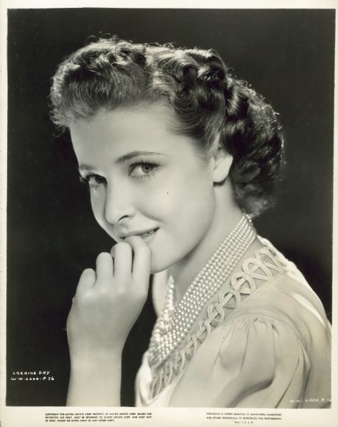 Head and shoulders portrait of actress Laraine Day taken during the filming of the movie "Foreign Correspondent." She is turned to the side and has her hand up to her mouth with a slight smile.