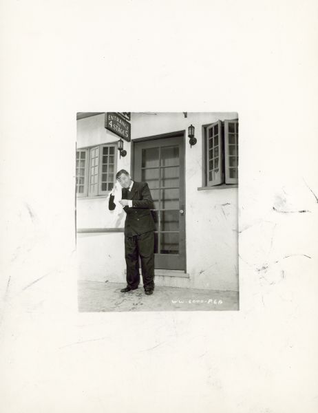 Herbert Marshall stands outside a stage door and dries off during the filming of the movie "Foreign Correspondent." He is wearing a suit and uses a towel to dry an ear.