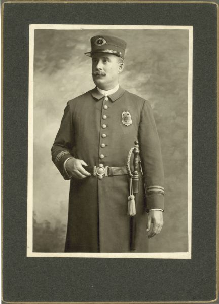 Three-quarter length studio portrait in front of a painted backdrop of a police officer in uniform.