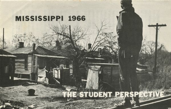 View from behind of a man standing on railroad tracks surveying a row of dilapidated shanties. Used on the cover of brochure with the title, 'Mississippi 1966: The Student Perspective.'