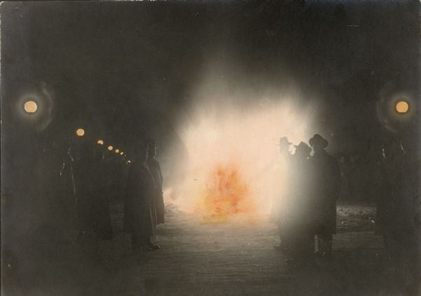 Men in hats are gathered around a nighttime bonfire, which was probably part of an anti-German demonstration.