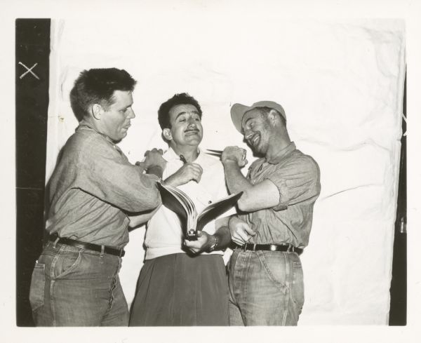 Actor Neville Brand, director Don Siegel, and another actor joke around on the set of the film "Riot in Cell Block 11." Brand holds Siegel as the other actor appears ready to stab Siegel in the neck with a knife.