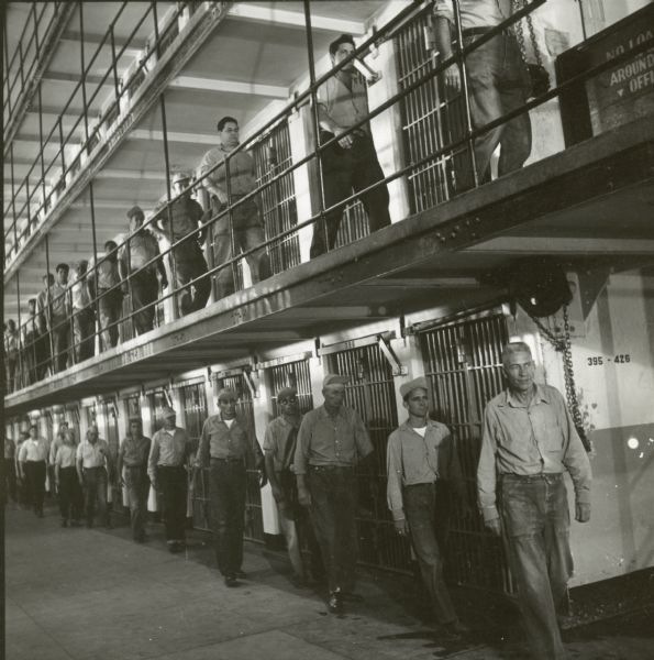 Prisoners are seen walking past cells on the set of the film "Riot in Cell Block 11." There are two lines of men — one on the first floor and another on the second floor.
