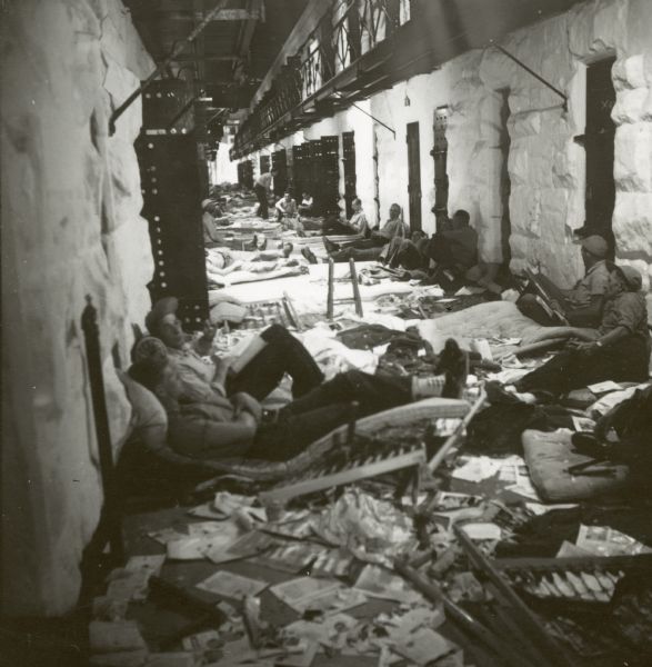 Prisoners sit on the floor outside of cells on the set of the film "Riot in Cell Block 11." Debris is on the floor.