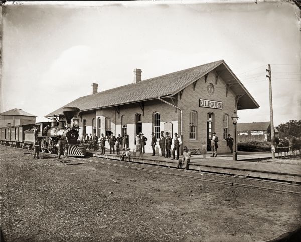 View towards a train at the Kilbourn City (now known as Wisconsin Dells) railroad depot, with a crowd of people on the platform.