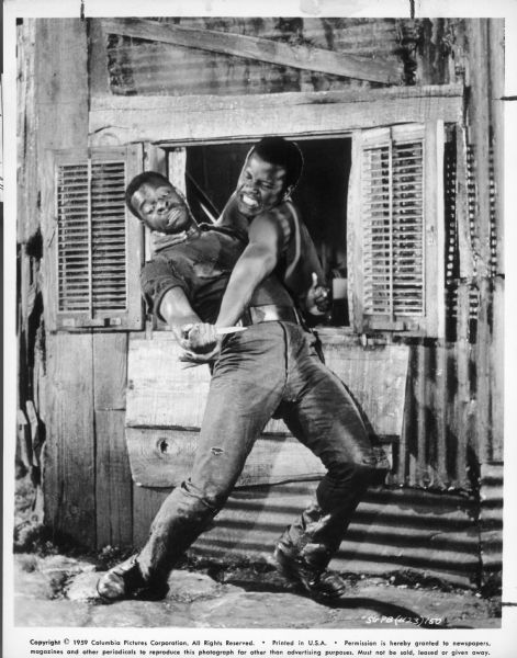Porgy (Sidney Poitier) and Crown (Brock Peters) fight one another. Poitier leans out a window and grabs Peters around the neck and wrist.  Peters is bending backwards and holds a knife.