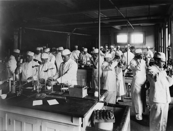 Large group of Dairy School students, all men, testing samples in the laboratory.