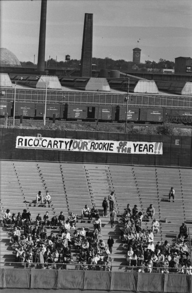 Elevated view of banner in the bleachers shows support for Braves outfielder Rico Carty for National League Rookie of the Year. A freight train, the Mitchell Park Domes, and the Allen Bradley Clock Tower are in the far background.