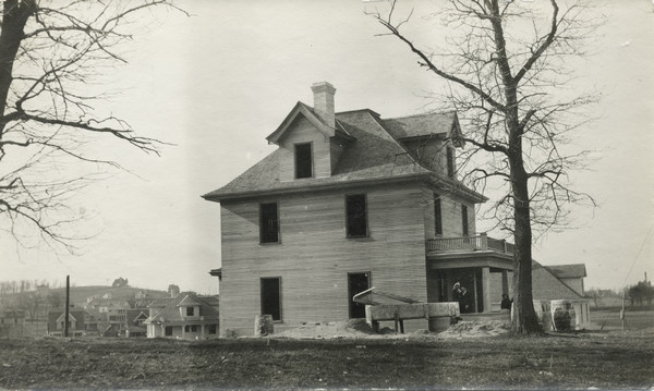 View of the house at 216 Campbell Street. Construction materials are piled about the property, suggesting it was recently built. A small group of people are posing on the porch. University Heights is the background.