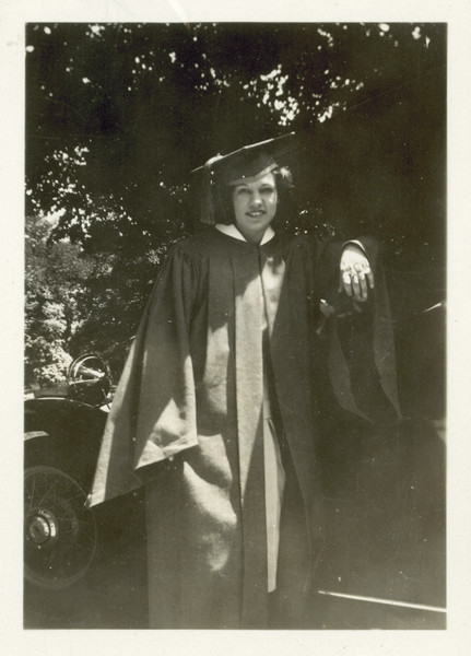 Alice Klusinski poses in her graduation cap and gown. She is leaning on an automobile and holding a rose in her left hand.