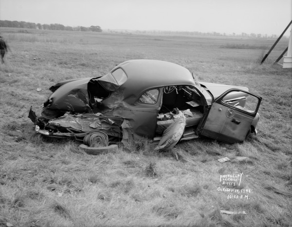 Accident scene involving a Findorff cement truck and a Studebaker coupe that were involved in a head-on crash on Highway 12 & 18 near the Royal Airport, showing heavy damage to the car. The occupants of the car were from the Milwaukee area. The driver of the truck was Phillip Crossen, 820 West Dayton Street. On the far right is what may be a billboard, and on the left a person is walking away.