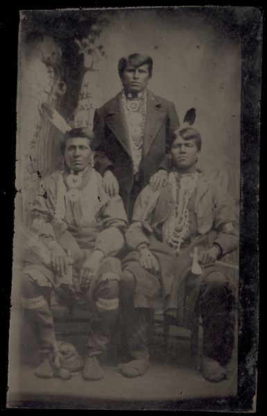 Studio group portrait in front of a painted backdrop of three men, two sitting, and one standing.