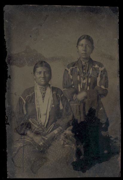 Studio portrait of two women, one sitting and one standing.