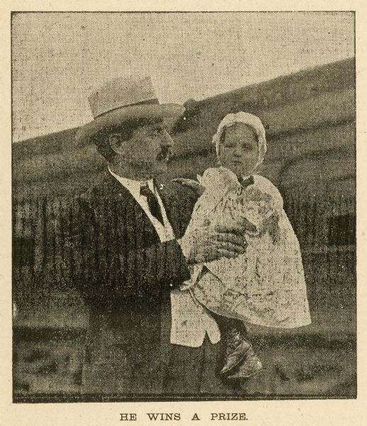 Newspaper clipping of a man holding a small child in his arms who arrived on the orphan train for adoption. The caption is: "He Wins A Prize."