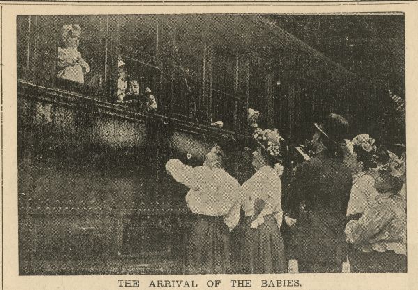 Newspaper clipping of prospective parents looking up at children in the windows of the orphan train. The caption reads: "The Arrival of the Babies."