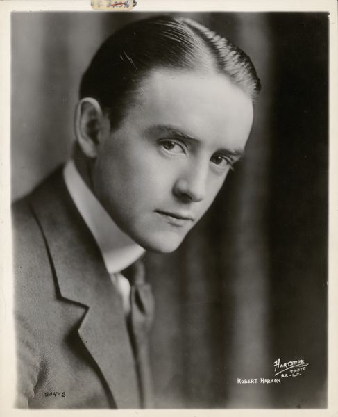 Quarter-length portrait of actor Robert Harron. He is wearing a suit and tie and is leaning forward. The name of the studio and his name are printed in the lower right corner.
