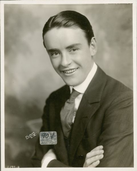 Waist-up publicity portrait of actor Robert Harron. His arms are crossed and he is smiling at the camera. He is wearing a suit coat, vest, tie and dress shirt.
