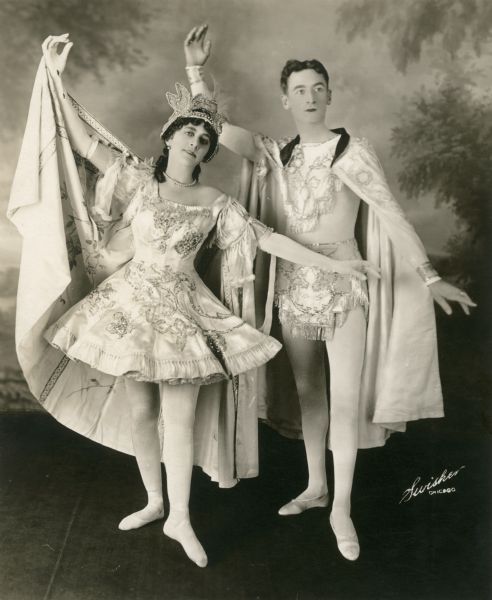 Rose Dockrill, daughter of Barnum and Bailey Circus equestrian Elise Dockrill, and her husband George E. Holland, son of George F. Holland, who was a famous equestrian and circus owner. They are dressed in circus costumes and posing elegantly in front of a painted backdrop.