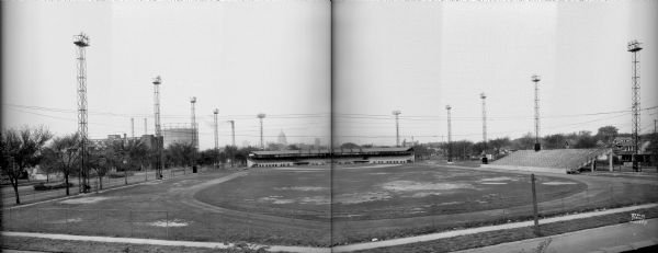 Composite of two negatives of Breese Stevens Athletic Field with lights on tall poles. On the left, view is of the Simon Brothers Wholesale Grocery Warehouse, 901 E. Washington Avenue, power plant chimney and storage tank in the background. The Wisconsin State Capitol is in the background in the center. On the right the view is looking toward E. Mifflin Street. Houses are in the background.