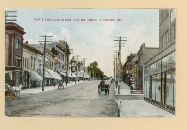 View down of Main Street from along right-side curb. Horse-drawn vehicles are on the street, and pedestrians are on the sidewalks. Storefronts are on both sides of the street. Caption reads: "Main Street, Looking East from the Bridge, Stoughton, Wis."
