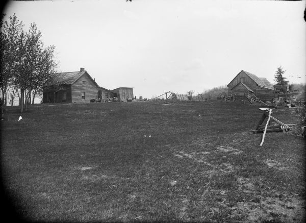 View across grassy field towards a farmhouse and weathered farm buildings.