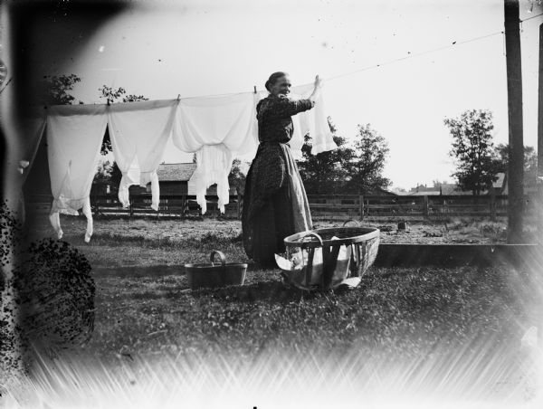 A woman hangs laundry on a clothesline in a yard.