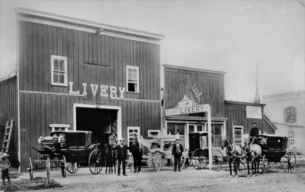 Men posed in front of a livery barn and horse sales stable.