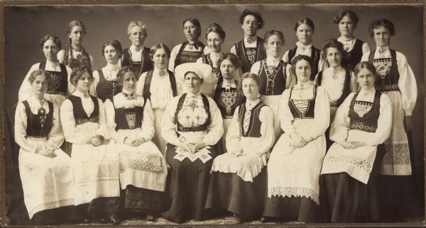Group portrait of a sewing circle of young girls and women wearing Norwegian costumes.