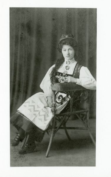 Full-length portrait of Lina Hveem, mother of Odva Haug, seated in a chair and wearing Norwegian costume for 17th May, just after arriving in the United States from the Toten area of Norway.