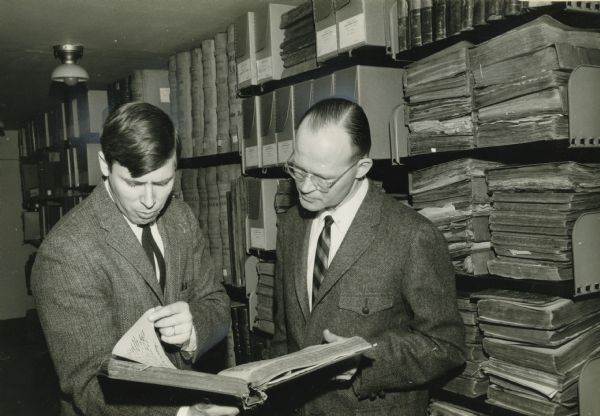 The caption with this photograph reads: "Dr. Walter Peterson (right), professor of history at Lawrence University, Appleton, with F. Gerald Ham, Wisconsin state archivist, examining the records of Milwaukee Downer College on deposit in the State Historical Society's area research center at the University of Wisconsin at Milwaukee." F. Gerald Ham was the State Archivist of Wisconsin from 1964 to 1989 and the head of the Division of Archives and Manuscripts at the State Historical Society of Wisconsin. F. Gerald Ham wrote a number of influential practical and academic works on the field of archives during his career.