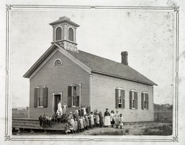 Exterior view of the school at Brothertown. with students and teacher posed outdoors around the front steps.