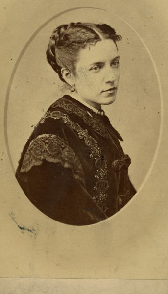 Oval-framed waist-up portrait of Emma Fuller Stevens wearing an elaborate dress. Her hair is braided and she is wearing earrings.