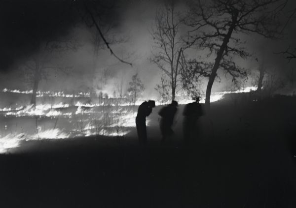 View of three people silhouetted against the advancing edge of a brush fire.