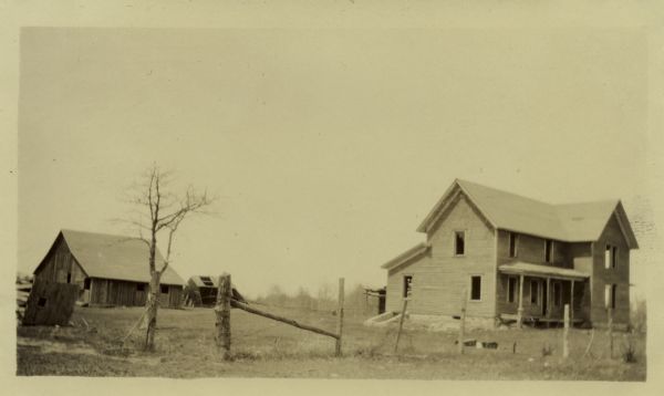 View of an abandoned home and barn behind a post fence.