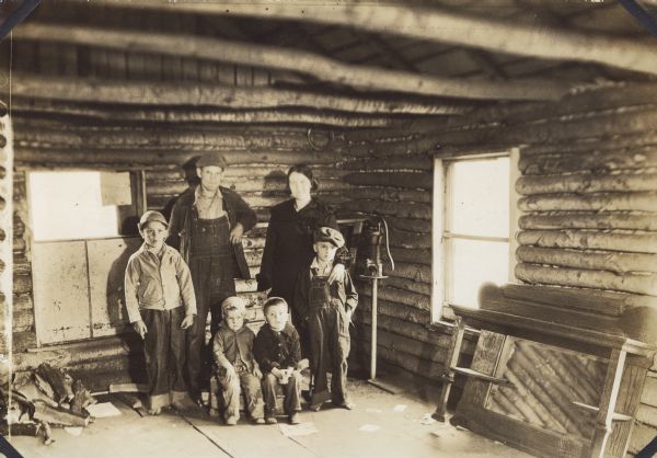 Portrait of the Brundage family in their old log cabin home. They are, left to right, standing: Robert (10), Walter, Thelma, Bruce (7), and seated: Victor (2) and Marvin (3). There is a pump for water in the corner of the room.