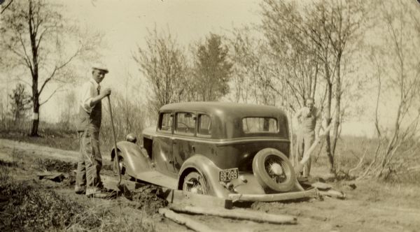 Will Morrow (in a hat) and J.T. Samson, United States Resettlement Administration field workers, using shovels and boards to extract a vehicle from a muddy road.