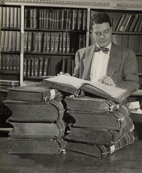 Dr. Clifford L. Lord posed standing examining large bound volumes from the Cudahy papers in the collections of the State Historical Society of Wisconsin.