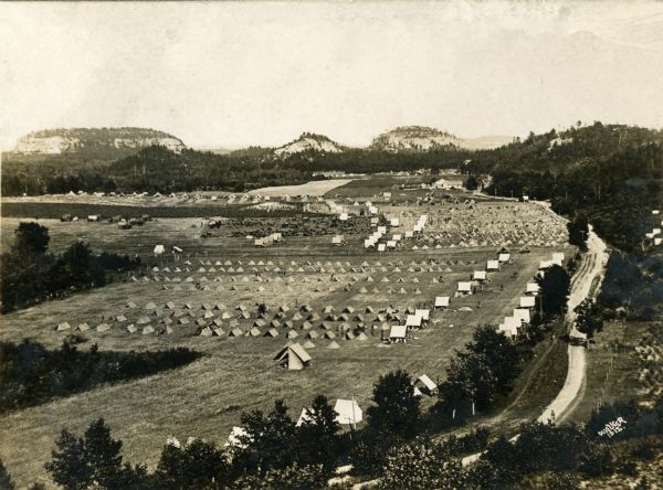 Bird's-eye view of Camp Douglas with several tents set up at center. Surrounding bluffs are in the distance.