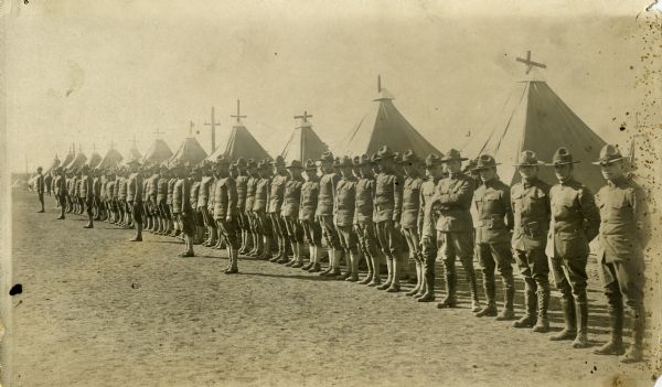 View of a long line of soldiers standing in rows in front of tents at Camp Douglas.