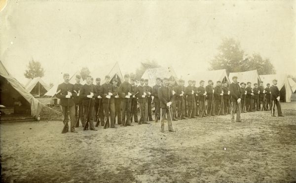 Outdoor group portrait of Company M, 3rd Wisconsin National Guard posed in front of tents at Camp Douglas.