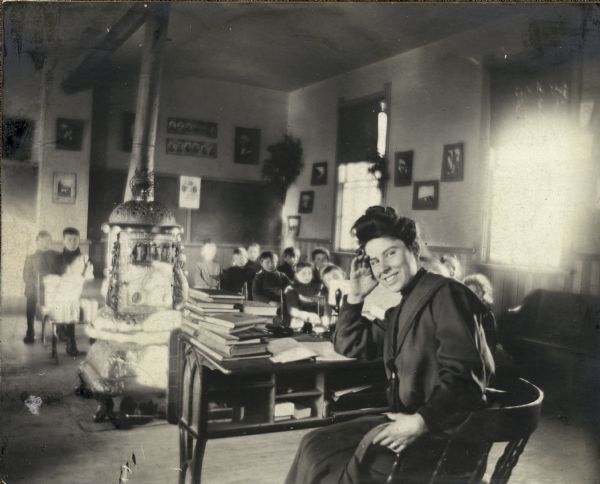 Informal portrait of Katherine Morrissey Dodge Cook seated at a desk in front of a classroom full of students.